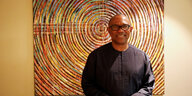 Peter Obi trägt Brille und steht vor einem bunten Kunstwerk.