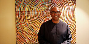 Peter Obi trägt Brille und steht vor einem bunten Kunstwerk.