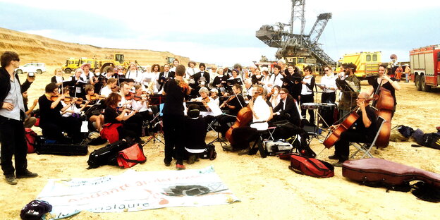 Ein Orchester stimmt Instrumente, ein Schild „Leben statt Kohle“ daneben