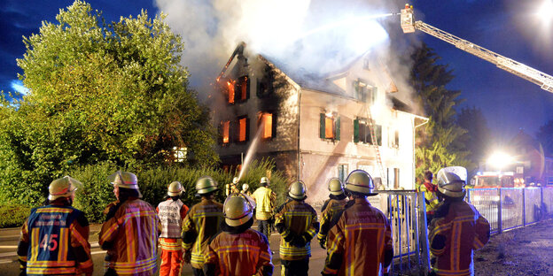 Feuerwehrleute vor einem brennenden Haus. Feuerwehrleute vor einem brennenden Haus.