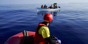 Eine Person auf einem Rettungsboot nähert sich einem überfüllten Holzboot