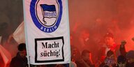 Fans in der Kurve mit Pyrotechnik und einem Transparent mit Hertha-Emblem