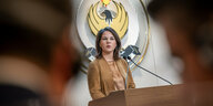 Außenministerin Annalena Baerbock am Rednerpult, hinter ihr das Wappen Kurdistans