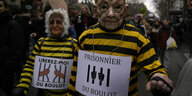 Zwei Demonstrant*innen in Gefängniskleidung protestieren gegen Gefangenschaft durch Arbeit.