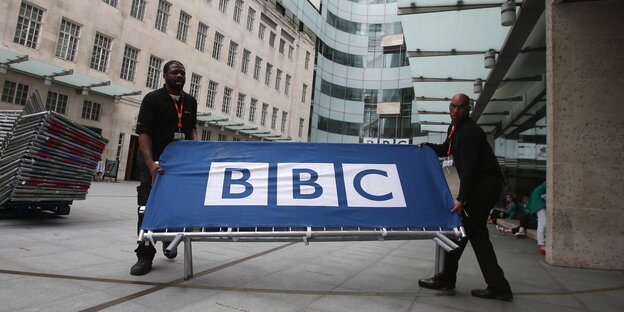 Zwei Männer tragen ein BBC-Schild Zwei Männer tragen ein BBC-Schild