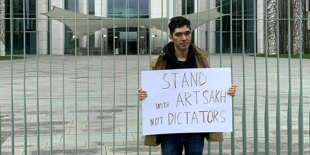 Arshak Makichchyan stands in front of the Federal Chancellery in Berlin with a sign: 