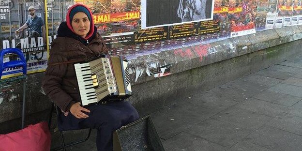 Dorina sitzt mit ihrem Akkordeon unter der S-Bahn-Brücke