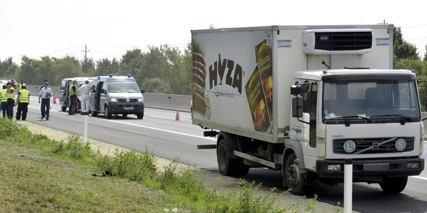 Der Lastwagen, in dem tote Geflüchtete gefunden worden sind, steht am Autobahnrand. Im Hintergrund Polizei. Der Lastwagen, in dem tote Geflüchtete gefunden worden sind, steht am Autobahnrand. Im Hintergrund Polizei.