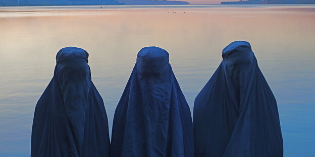 Three people with burqas in front of a lake