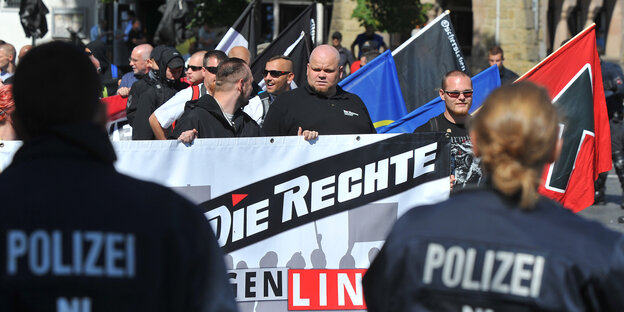 Neonazis halten ein großes Transparent und Fahnen, im Vordergrund die Silhouetten von PolizistInnen Neonazis halten ein großes Transparent und Fahnen, im Vordergrund die Silhouetten von PolizistInnen