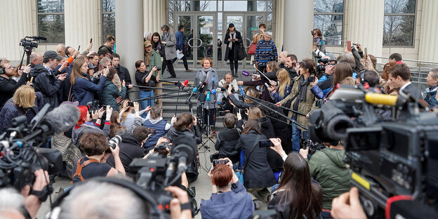 Journalists stand in front of a courthouse in Moscow, a woman speaks into a microphone