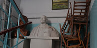 Lenin-Büste in einem Treppenhaus, daneben aufgestapelte Stühle, eine weitere Büste, eine Aluleiter