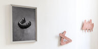 Blick in die Ausstellung "Außendran die Beine". Links an der Wand hängt eine Schwarz-Weiß-Fotografie von Clara Bahlsen. Darauf ist Sand in einer U-Form geschichtet, auf dem Sand sind rundum kleine weiße Steinchen verteilt. Die Arbeit trägt den Titel "Zähn
