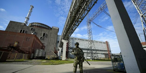 A uniformed soldier stands in front of a power plant
