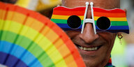Ein Mann mit einer Regenbogenbrille und einem Regenbogenfächer lächelt in die Kamera