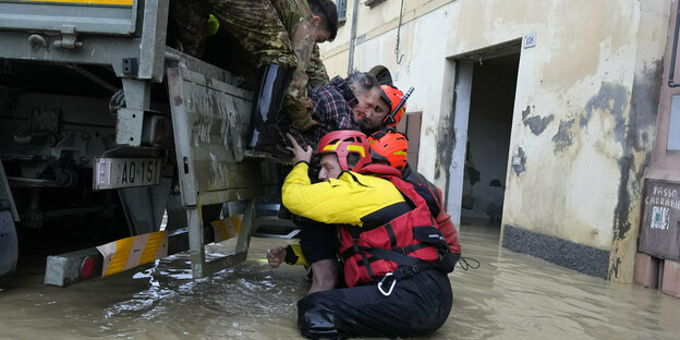 Firefighters stand waist-deep in water and push a man onto the back of a truck
