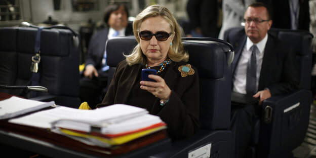 Hillary Clinton sitzt mit Sonnenbrille in einem Flugzeug und schaut auf ihr Handy Hillary Clinton sitzt mit Sonnenbrille in einem Flugzeug und schaut auf ihr Handy
