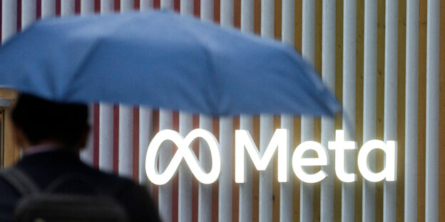 Ein Mann mit einem Regenschrim läuft am Meta - Logo vorbei