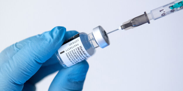 Eine spritze mit Impfstoff wird aufgezogen und von einem blauen Gummihandschuh gehalten