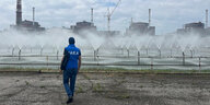 Wassersprenkler vor einer Industrieanlage, ein Mann mit blauem Oberteil und IAEA Aufschrfit