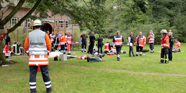Feuerwehrmenschen auf einer Wiese vor einem reetgedeckten Haus Feuerwehrmenschen auf einer Wiese vor einem reetgedeckten Haus