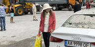 Frau mit Hut und Einkaufstauschen neben zerstörtem Auto