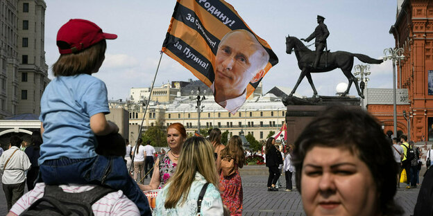 Eine Fahne mit Putins Portrait , ein Reiterdenkmal am Kreml , ein Kind auf den Schultern eines Mannes