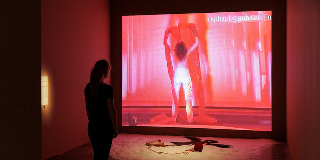 Blick in die Ausstellung, eine Frau vor einem großen Bildschirm, auf dem eine Arbeit Rosenbachs zu sehen ist