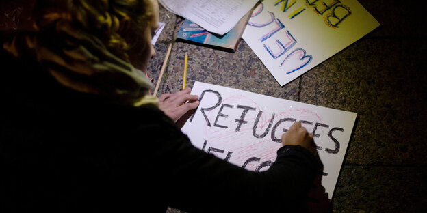 Eine Frau schreibt „Refugees welcome“ auf ein Schild Eine Frau schreibt „Refugees welcome“ auf ein Schild