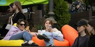 Junge Frauen sitzen mit ihren Smartphones im Freien in einem Cafe
