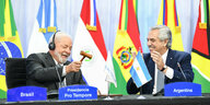 Luiz Inacio Lula da Silva aus Brasilien und der argentinische Präsident Alberto Fernandez sitzen gut gelaunt auf einem Podium, Lula mit dem Hammer in der Hand und Fernandez lacht