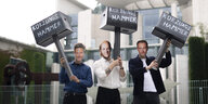 Drei Demonstrierende mit Habeck-, Scholz- und Lindnermasken stehen vorm Bundeskanzleramt, in den Händen Hammerattrappen mit der Aufschrift „Kürzungshammer“