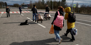 Kinder gehen mit Eltern und Gepäck übr eine Straße auf der ein Hund liegt