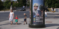 Eine Werbesäule mit Soldaten abgebildet, daneben läuft eine Frau mit zwei Kindern vorbei