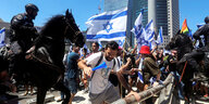 Ein berittener Polizist reitet in eine Menschenmenge, die mit israelischen Flaggen vor einer Absperrung steht