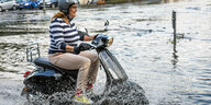 Frau auf Motorroller fährt durch Hochwasser