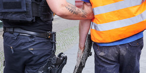 Ein Polizist führt einen Aktivisten der Letzten Generation von der Straße, an dessen Hand noch Asphalt hängt.