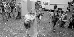 Eine Frau in einem Kleid tanzt zwischen anderen Personen auf einer staubigen Wiese