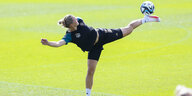 Eine Fußballerin streckt sich auf akrobatische Weise, um einen Ball mit der Hacke in der Luft zu spielen.