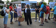 Menschen stehen vor einer Stellwand zum Gewässerschutz, ein Mann und eine Frau in schwarzen Shirts erklären etwas