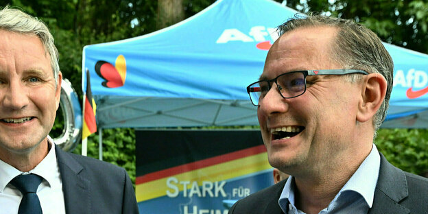 Björn Höcke, Vorsitzender der AfD Thüringen und Tino Chrupalla, AfD-Bundesvorsitzender, stehen lachend an einem Wahlkampfstand.