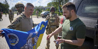 Ukrainischer Präsident Selenski mit Soldaten, die ihm eine blau-gelbe Flagge zeigen.