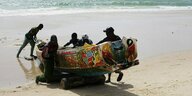 Männer schieben eine Piroge am Strand von Saint Louis, Senegal