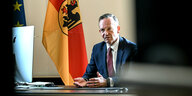 Verkehrsminister Volker Wissing sitzt an seinem Schreibtisch im Ministerium und hinter ihm hängt eine große Deutschlandflagge