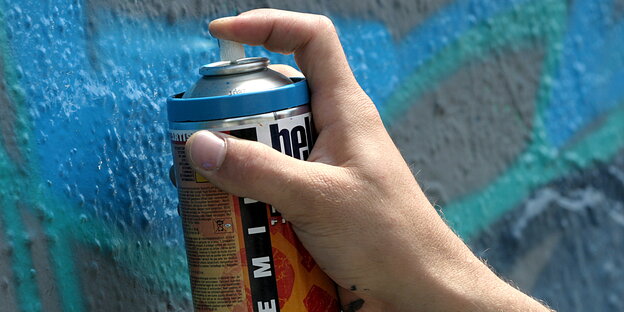 Eine Hand sprüht blaue Farbe auf eine Mauer Eine Hand sprüht blaue Farbe auf eine Mauer