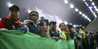 Die Teilnehmer stehen in einer Reihe, lauschen einer Rede während einer Zeremonie und halten gemeinsam ein grünes Stoffbanner