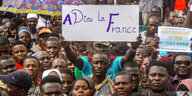 Ein Mann hält in einer protestierenden Menge in Niger ein Schild hoch: A Dieu la France