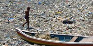 Eine Person läuft durch Plastikmüll an einem Strand.