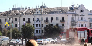 Eine Häuserfront mit beschädigten Fassaden und Dächern. Ein Feuerwehrauto fährt vorbei