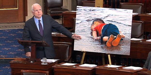 Senator John McCain steht neben einem Bild von Aylan Kurdi, dem toten syrischen Jungen, der ertrunken war Senator John McCain steht neben einem Bild von Aylan Kurdi, dem toten syrischen Jungen, der ertrunken war